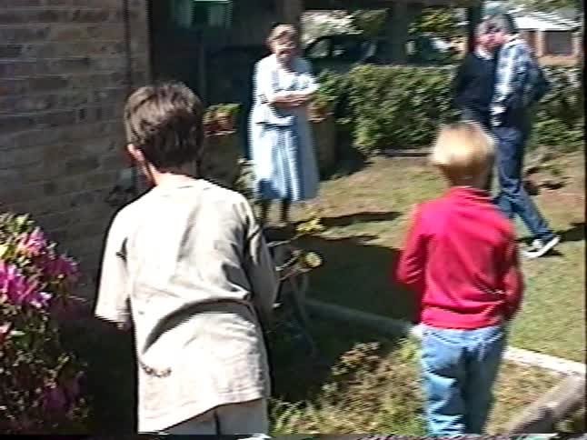 Vintage home video of two young boys playing in a backyard during a family gathering on a sunny day