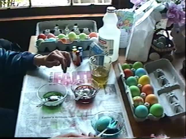 Nostalgic home video footage shows hands dyeing colorful Easter eggs at a table covered in newspaper
