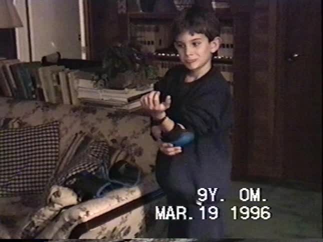 A young boy smiles as he gets ready to go rollerblading, putting on his elbow pads and wrist guards in this vintage 1996 home video