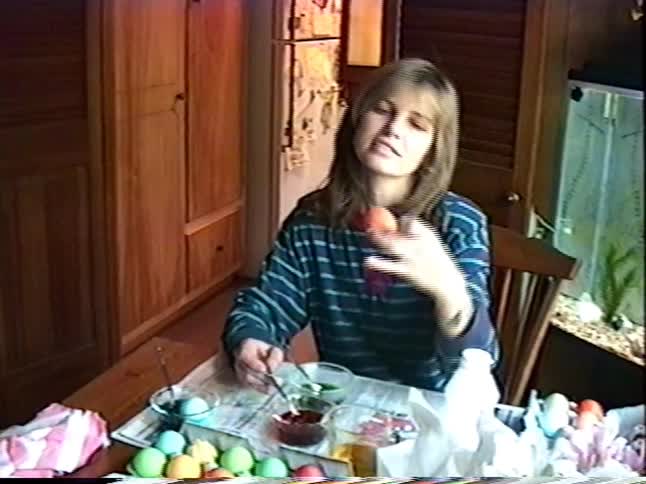 Vintage VHS footage shows a woman dyeing colorful Easter eggs at a table in her home