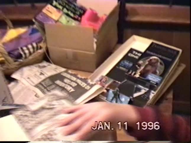 A cute little boy in a colorful party crown examines his birthday presents wrapped in newspaper in a nostalgic home video from 1996