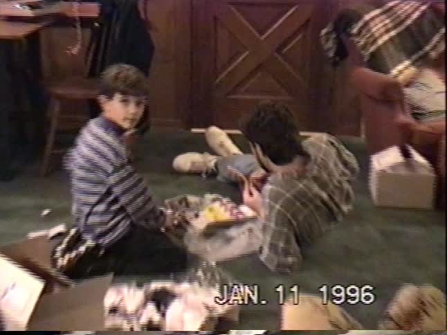 A grainy VHS home movie captures two young brothers playing on the living room floor in 1996