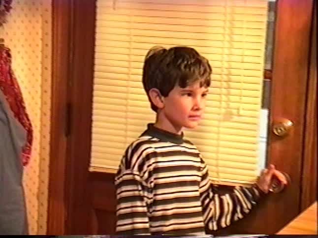 Nostalgic handheld home movie shot of a young boy waiting by the back door in a cozy 1990s kitchen