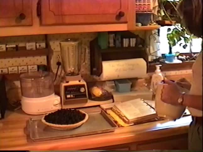 Vintage home movie captures a woman following a recipe to bake a pie in her sunlit kitchen