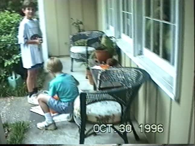 A vintage 1996 home video shows two young boys on a porch carving pumpkins for Halloween