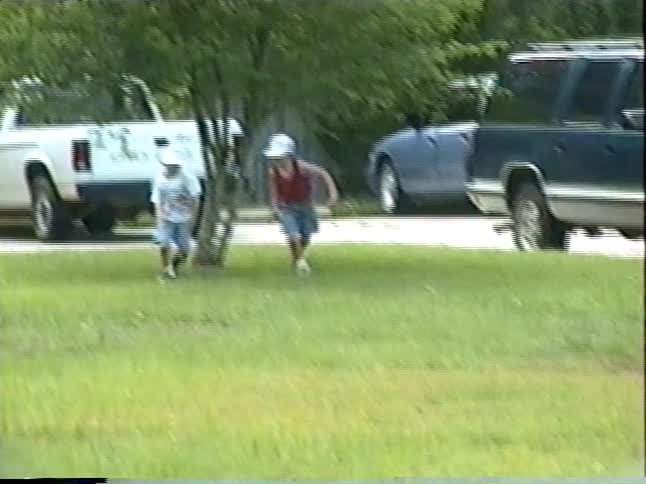 Two young boys in baseball caps have a race across a large grassy field on a summer day