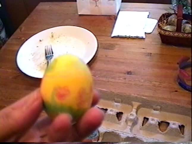 A vintage home video shows a close-up of a hand displaying several colorful, freshly dyed Easter eggs