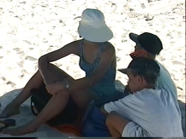 Vintage footage shows a mother and her two sons relaxing on a busy beach with rows of green umbrellas
