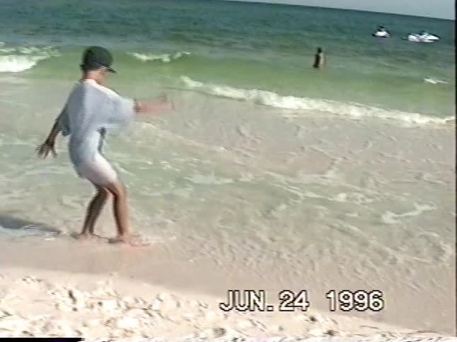A young boy in a baseball cap smiles and shows off a seashell on a sunny beach before playing in the sand and waves