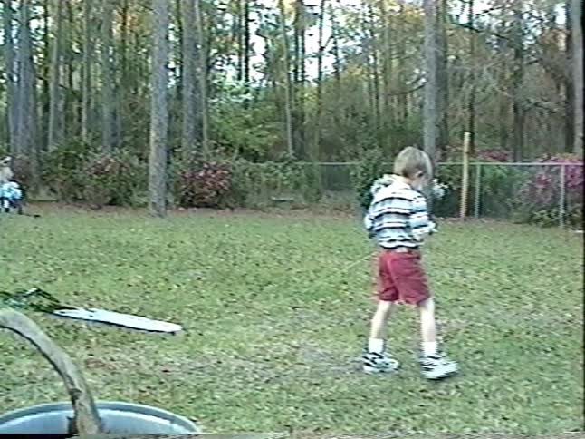 Vintage home movie captures two young brothers running through a wooded backyard as they struggle to fly a colorful kite