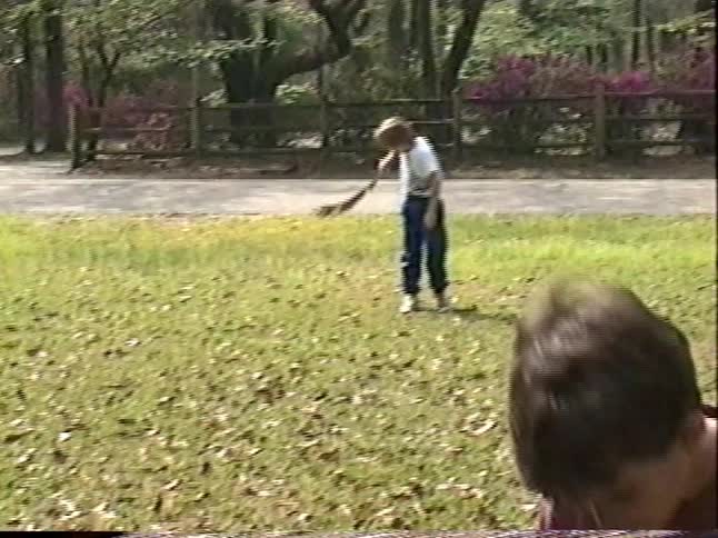 Vintage VHS footage captures a suburban home's yard with blooming azaleas and children playing outside