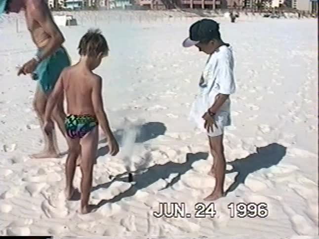 Vintage 1996 home video shows two young boys lighting a smoke bomb on a sunny, white sand beach