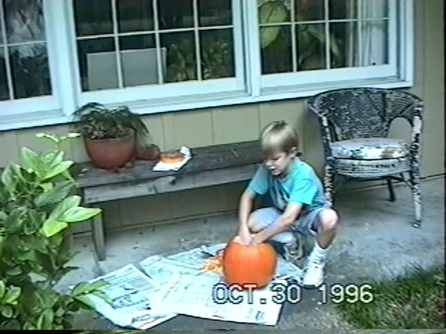 A young boy from a 1996 home video excitedly scoops the guts out of a large pumpkin on his family's patio for Halloween