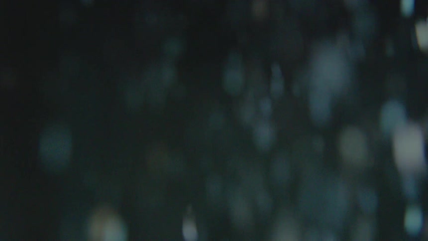 Abstract out-of-focus particles of dust and debris float and fall in slow motion against a dark background