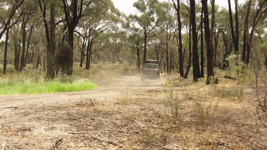 A rugged four-wheel-drive vehicle kicks up dust as it travels down a dirt track in the Australian bush