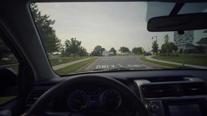 Driver's point of view pulling out of a parking lot and driving through a suburban town in slow motion