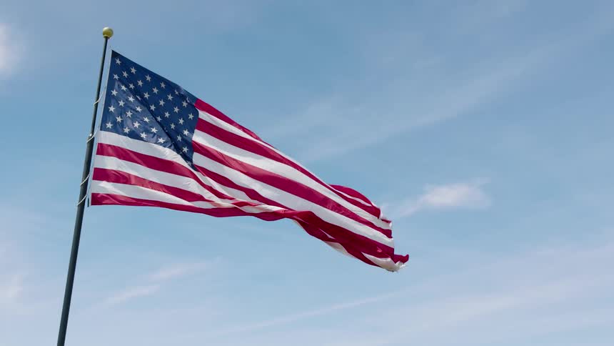 Low tilt up approach towards the American flag waving gracefully against a beautiful blue sky