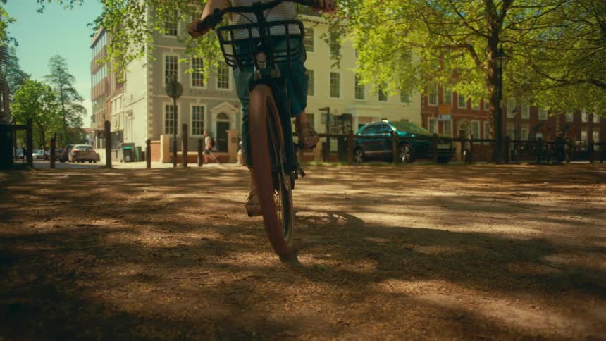 A young woman wearing a helmet enjoys a leisurely slow-motion bike ride through a sunny urban park