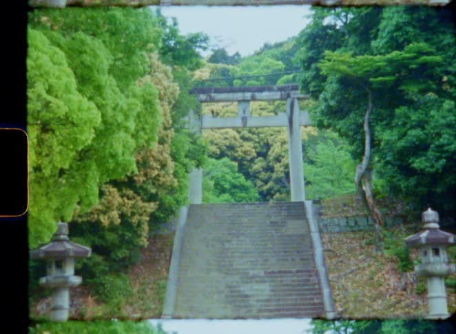 Vintage 8mm film of a stone torii gate at the top of a long staircase in a lush green Japanese forest