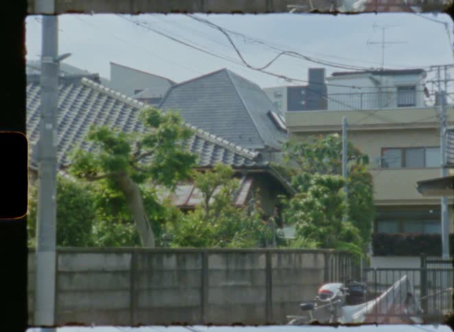 Vintage 8mm film captures a still scene of a residential street in Japan with lush trees and power lines