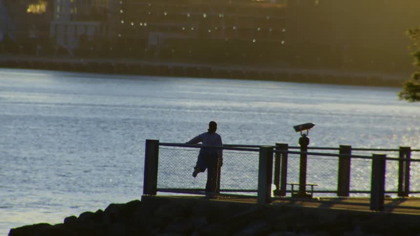 A silhouetted person stands alone on a pier at sunrise, peacefully looking out over the water