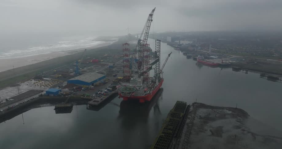 Aerial shot of a massive jack-up rig docked in an industrial seaport on a foggy and overcast day