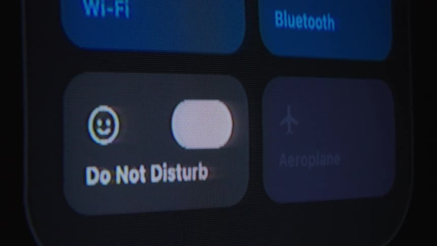 A close-up of a smartphone screen shows a user turning on the Do Not Disturb mode in the control center
