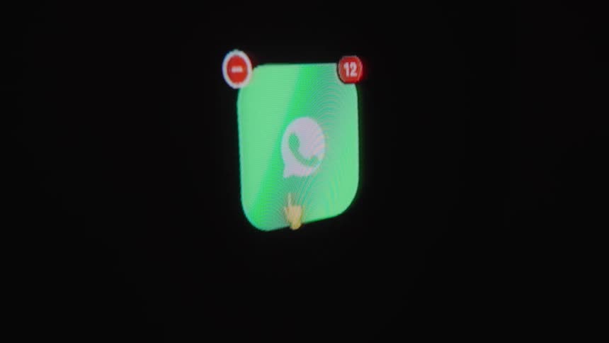 A person uninstalls the WhatsApp social media application from their phone's home screen