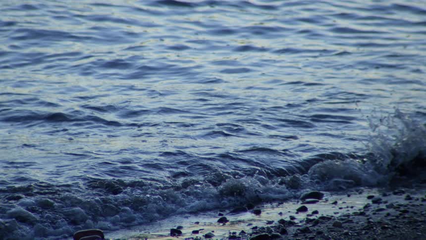 Mesmerizing slow-motion footage captures gentle blue waves lapping against a rocky shore