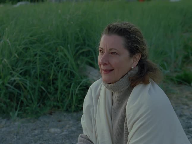 A pensive woman wrapped in a warm blanket finds a moment of peace while sitting on a beach at dusk