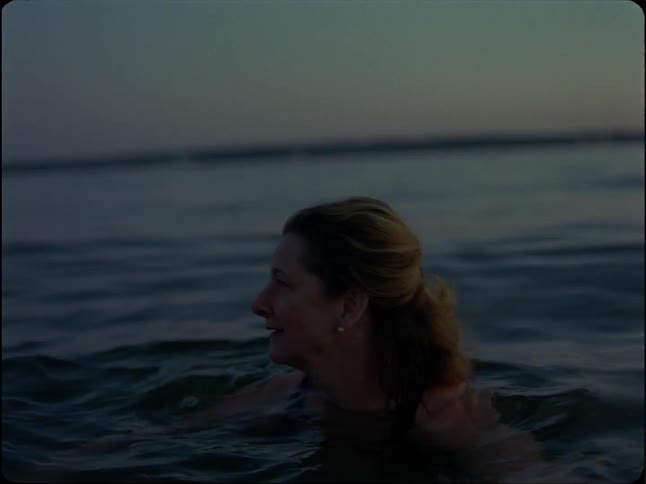 A contemplative woman peacefully swims in the ocean at dusk, smiling as she enjoys the calm water