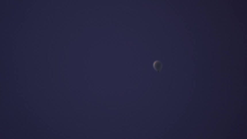 A single white balloon floats up and away into a solid dark blue background, eventually going out of focus