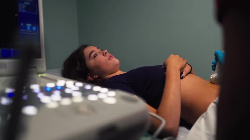 A young woman undergoes an abdominal ultrasound examination while lying on a table in a medical clinic