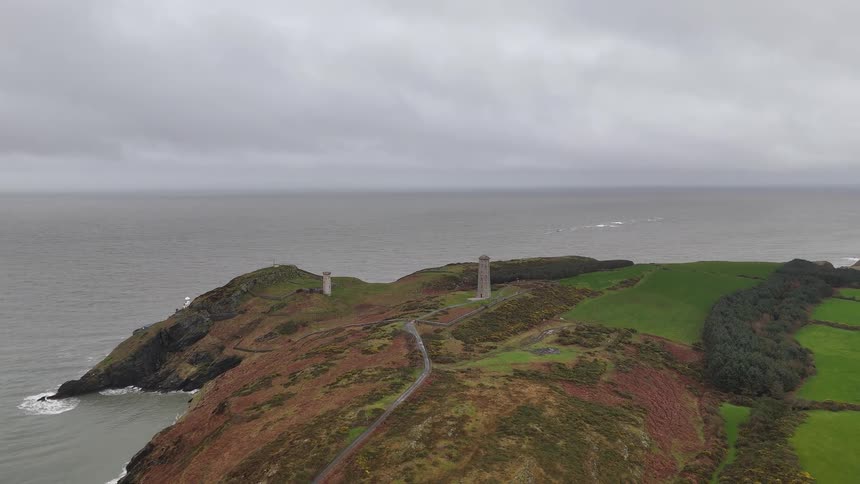 A slow pulling away aerial shot showcases the scenic lighthouses on the rugged headland of Wicklow, Ireland, overlooking the vast Irish Sea on a cloudy day