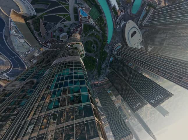 A vertiginous aerial shot creates a surreal tiny planet effect as it flies over the top of a Dubai skyscraper