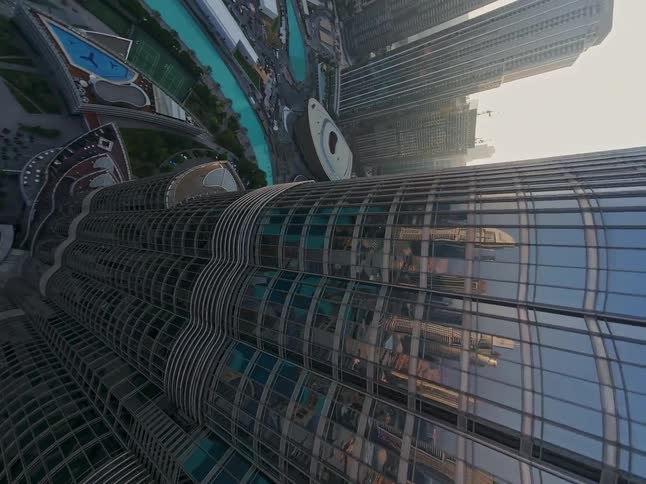 A dynamic FPV drone shot soars up the glass facade of the Burj Khalifa skyscraper, tilting up to reveal its full height against the Dubai cityscape