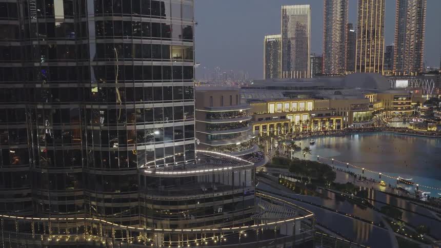 A sweeping aerial view reveals the illuminated cityscape of Downtown Dubai at dusk, showcasing the iconic Burj Khalifa and bustling waterfront
