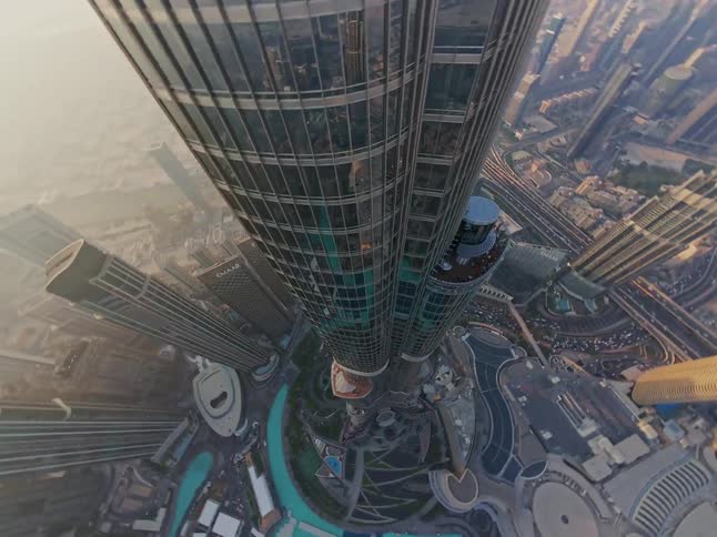 A stunning and dizzying top-down aerial shot circling the spire of the Burj Khalifa, overlooking the vast cityscape of Dubai