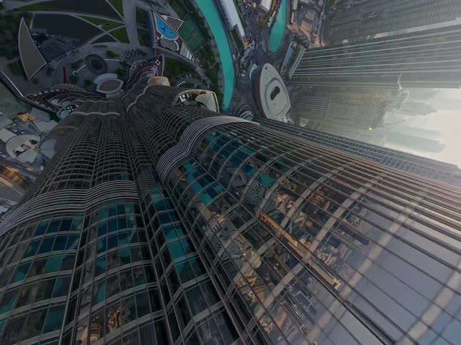 A dizzying aerial shot tilts down the side of the iconic Burj Khalifa, revealing the sprawling city of Dubai and its famous fountains below