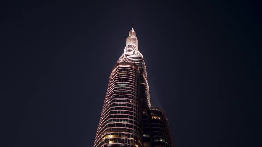 A slow zoom out from the illuminated Burj Khalifa reveals its towering height against the vast, dark night sky