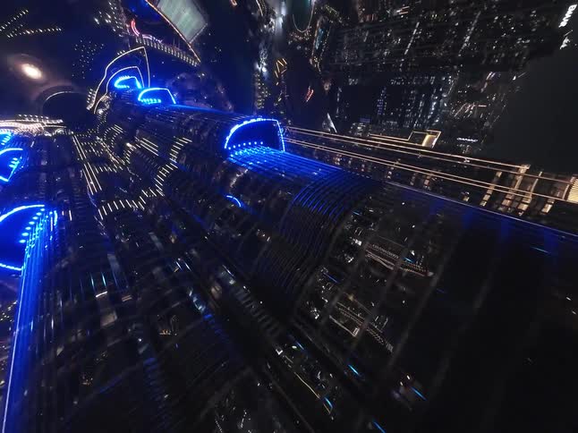 Tilting up the side of the illuminated Burj Khalifa reveals a stunning top-down aerial view of the Dubai cityscape at night