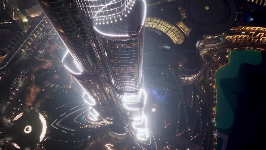 A mesmerizing top-down aerial view of a futuristic skyscraper illuminated against the vibrant city lights below at night