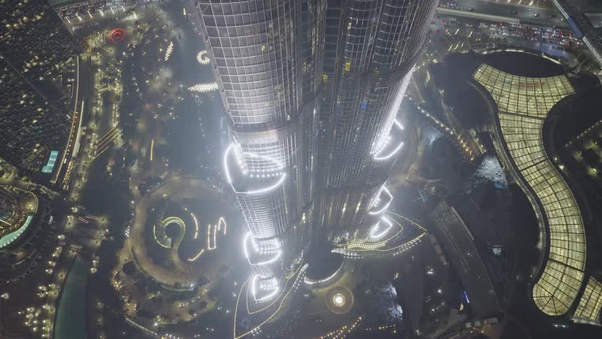 An incredible top-down aerial view slowly zooms out from the illuminated Burj Khalifa skyscraper in Dubai at night