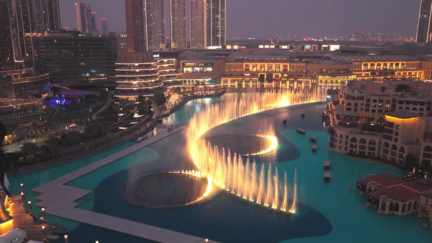An elevated view of the spectacular Dubai Fountain light and water show at dusk with the UAE flag in the foreground
