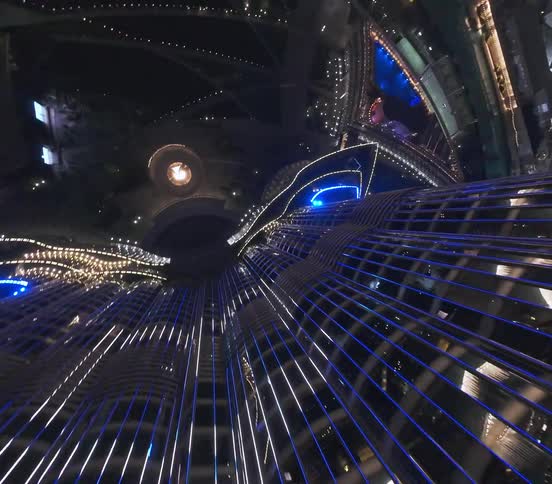 A thrilling FPV drone dives down the glittering face of the Burj Khalifa at night, revealing the spectacular Dubai Fountain show below
