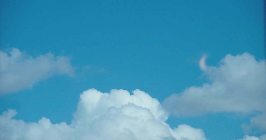 A faint crescent moon is visible in the bright blue daytime sky above large white clouds