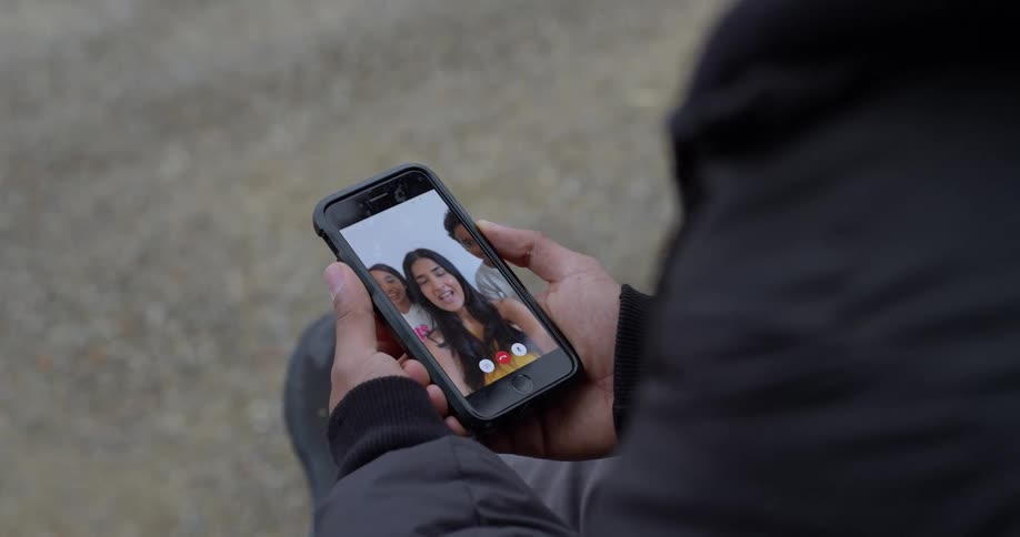 Over the shoulder view of a person holding a smartphone and having a video call with a group of smiling friends