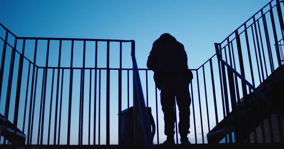A low angle shot shows the silhouette of a person standing on a metal stairwell against the deep blue dusk sky