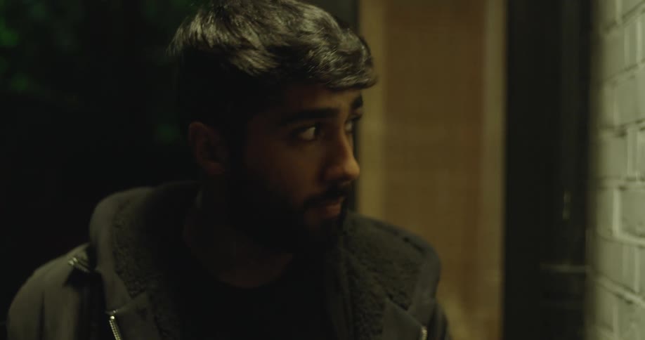 A young man wearing a jacket looks around suspiciously at night, then reacts with wide-eyed surprise