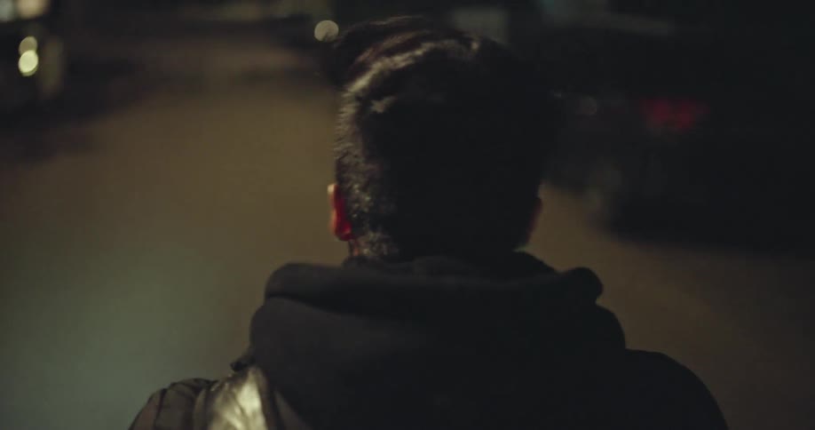 Over the shoulder shot of a man riding a motorcycle down a city street at night in slow motion